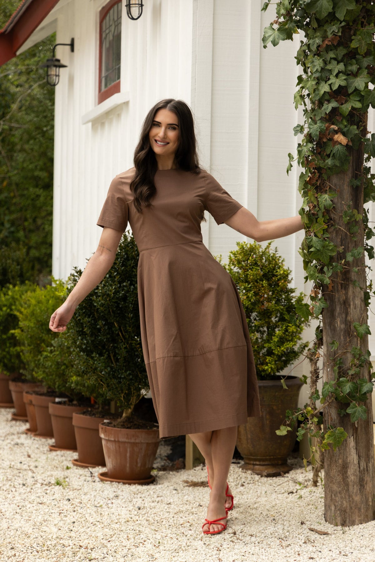 Brown short-sleeve midi dress with a seamed skirt, worn with red strappy heels